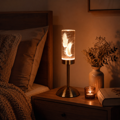 Lampe Little Daisy Plume sur une table de nuit en bois, diffusant une lumière douce et chaleureuse dans une chambre à coucher propice à la détente.