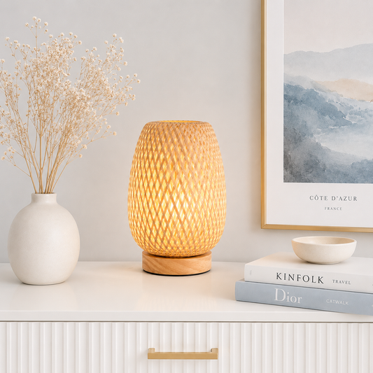 Lampe de table Tressa en bambou tressé à la main diffusant une lumière chaude et apaisante sur une console blanche dans un intérieur moderne et lumineux. Cette lampe décorative en bois naturel crée une ambiance chaleureuse et élégante, parfaite pour le salon, la chambre, l'entrée ou un coin lecture, avec une décoration haut de gamme aux tons greige et bleu poudre.