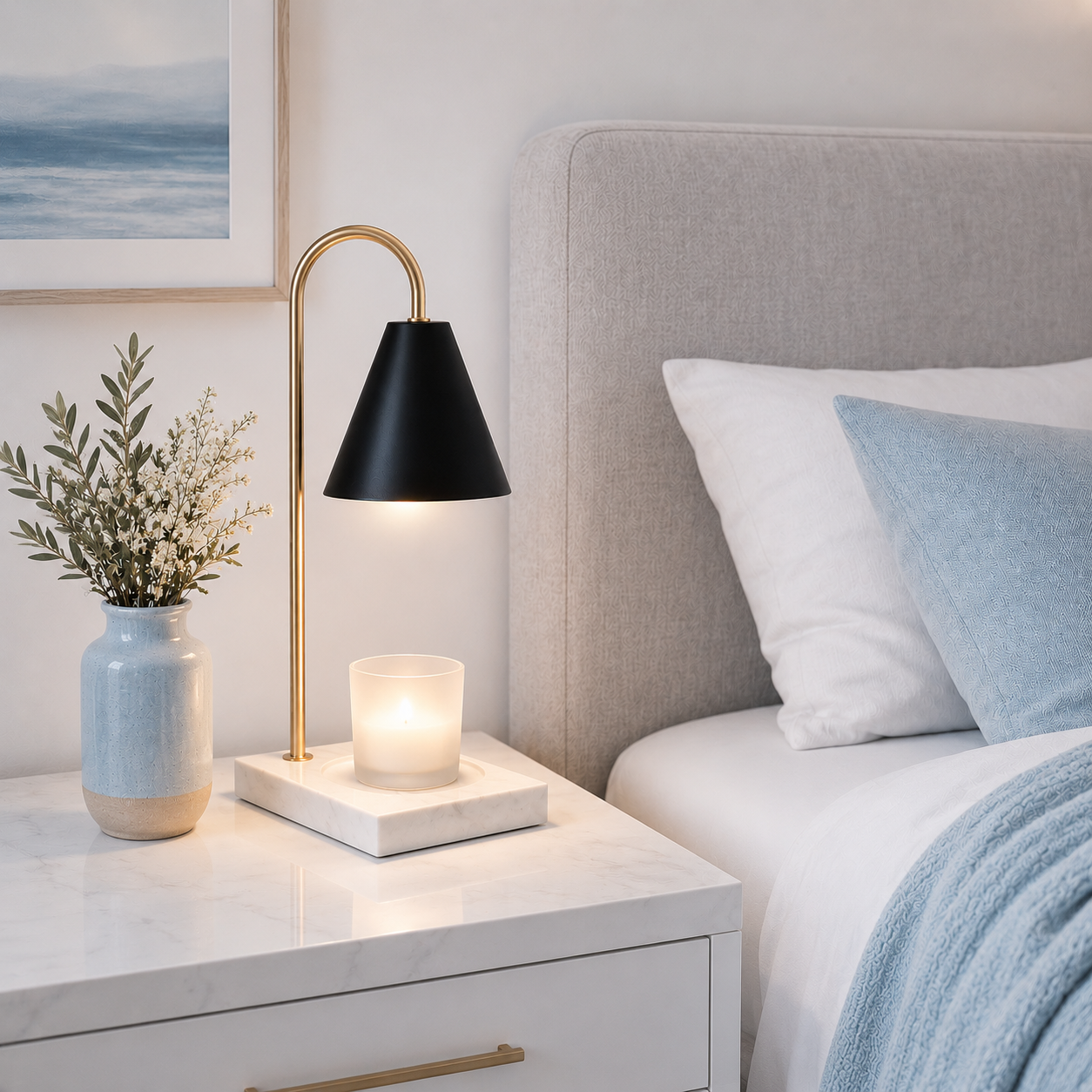 Lampe chauffante aromathérapie pour bougie parfumée diffusant une lumière douce sur une table de nuit blanche avec base en bois naturel, dans une chambre élégante avec coussin bleu poudre, tête de lit grise, décoration moderne et ambiance apaisante.