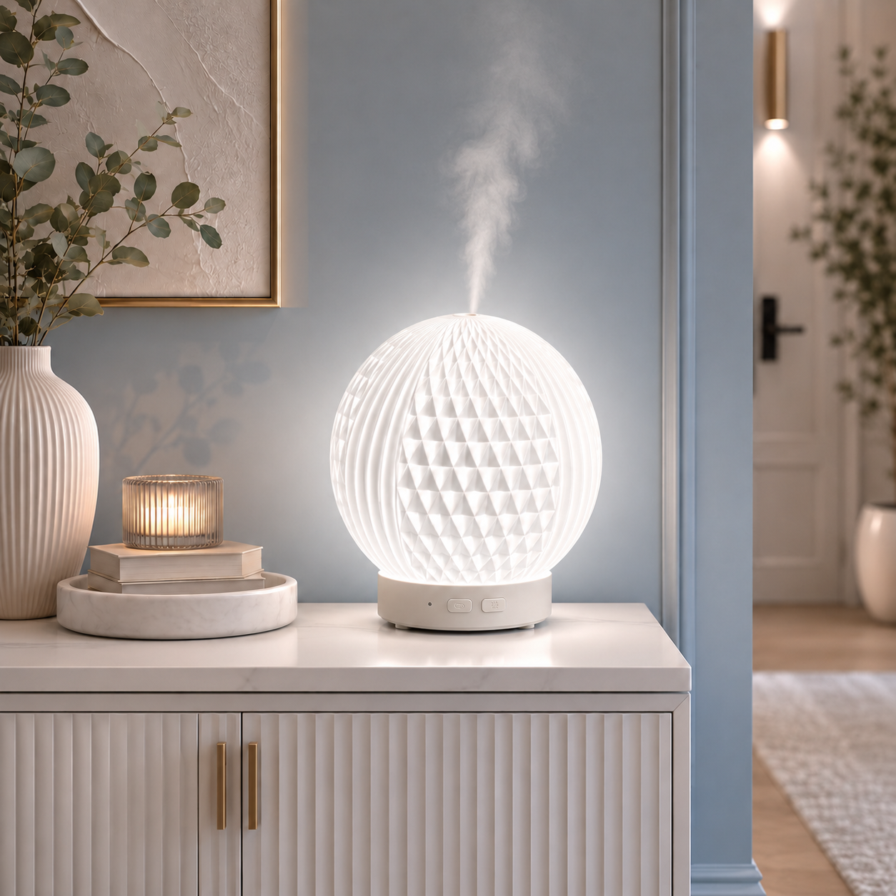 Diffuseur d'huiles essentielles LED Brise diffusant une fine brume sur une console blanche dans un hall d'entrée moderne aux tons greige et bleu poudre. Décoration élégante avec vase, bougie, tableau et mobilier haut de gamme créant une ambiance lumineuse, apaisante et raffinée.