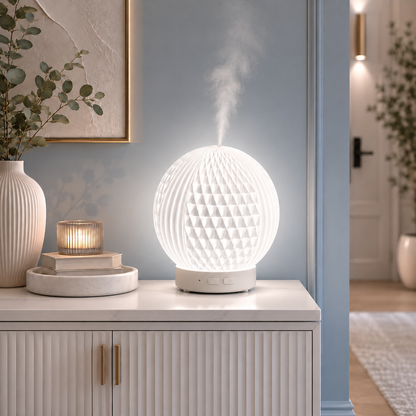 Diffuseur d'huiles essentielles LED Brise diffusant une fine brume sur une console blanche dans un hall d'entrée moderne aux tons greige et bleu poudre. Décoration élégante avec vase, bougie, tableau et mobilier haut de gamme créant une ambiance lumineuse, apaisante et raffinée.