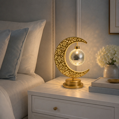 Lampe Lune Enchantée Boule Miroir dorée allumée sur une table de chevet blanche, éclairage LED décoratif créant une ambiance douce et apaisante dans une chambre élégante.