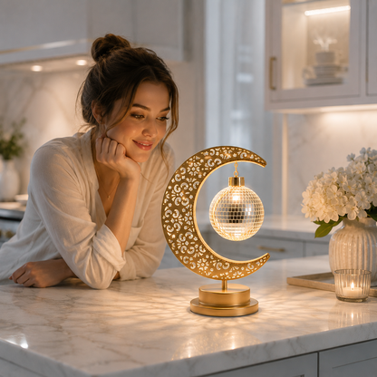 Femme admirant la Lampe Lune Enchantée Boule Miroir allumée sur un comptoir de cuisine moderne, éclairage LED décoratif créant une ambiance chaleureuse et élégante.