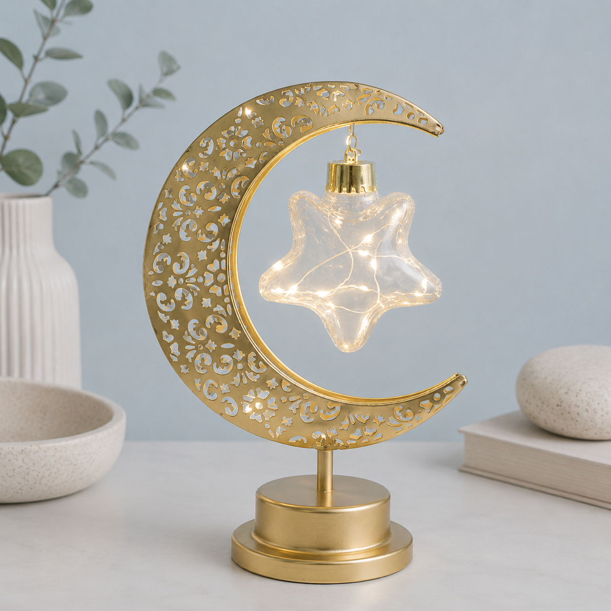 Lampe Lune Enchantée Étoile Lumineuse dorée allumée avec étoile lumineuse suspendue, éclairage LED décoratif, design élégant sur fond greige bleu poudre, idéale pour le salon, la chambre ou un bureau.