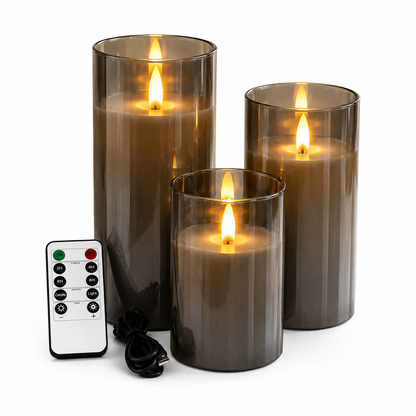 Ensemble de 3 bougies LED rechargeables en verre fumé avec effet flamme réaliste, présenté sur fond blanc avec télécommande multifonction et câble USB inclus. Les trois bougies décoratives de différentes hauteurs créent une ambiance chaleureuse et élégante tout en offrant une utilisation sécuritaire grâce à leur fonctionnement sans flamme, leur minuterie programmable et leur intensité lumineuse réglable.