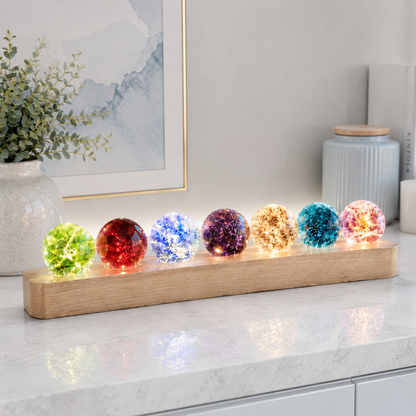 Gros plan du kit de sphères lumineuses décoratives Lumina posé sur un comptoir en quartz blanc, diffusant une lumière douce et colorée dans un intérieur moderne et raffiné aux tons greige et bleu poudre.