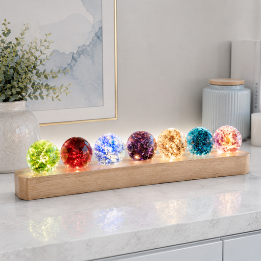 Gros plan du kit de sphères lumineuses décoratives Lumina posé sur un comptoir en quartz blanc, diffusant une lumière douce et colorée dans un intérieur moderne et raffiné aux tons greige et bleu poudre.